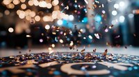 Scattered metallic confetti on dark surface with blurred bokeh lights creating festive atmosphere. Macro shot captures shimmering pieces in motion against blurry background.
