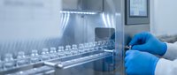 Laboratory technician in blue gloves operating automated liquid handling system for pharmaceutical research and drug development in sterile environment.