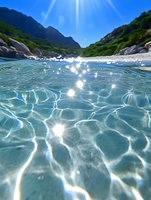 Crystal clear turquoise water with sunlight creating sparkles and caustic patterns on surface, mountains and green cliffs in background, split underwater view.