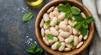 White lima beans in wooden bowl with fresh mint leaves and olive oil on dark stone background for healthy cooking and Mediterranean cuisine recipes.