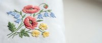 Delicate floral embroidery with pink poppies and blue flowers on white fabric showcasing traditional needlework craftsmanship for textile and craft projects.