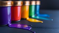 Vibrant paint jars arranged in rainbow spectrum with spilled purple paint on dark surface, selective focus on foreground creating artistic depth and composition.
