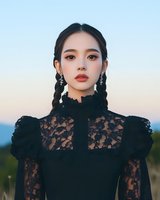 Young Asian woman in elegant black lace dress with braided hair and statement earrings posing outdoors during golden hour for fashion portrait photography.