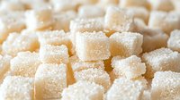 White sugar cubes covered in fine crystal sugar granules, macro food photography showing sweet ingredient texture in soft natural lighting.