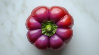 Fresh ripe purple bell pepper with distinctive flower-shaped segments viewed from above on white marble background, organic produce for healthy cooking.