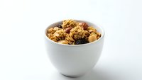 Homemade granola with nuts and dried fruits in white ceramic bowl on clean background for healthy breakfast and snack concepts.