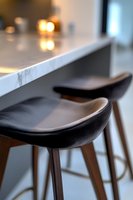 Modern black leather bar stools with wooden legs against marble countertop, soft bokeh lights in background create luxurious kitchen atmosphere.