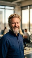Confident mature Caucasian businessman with curly hair and beard smiling in modern office environment for corporate leadership and professional success.