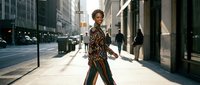 Young African American businesswoman walking confidently down urban city street in professional attire during golden hour sunlight.