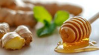 Fresh ginger root with honey dripping from wooden dipper on white wooden surface, garnished with mint leaves, macro food photography.