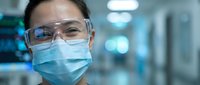 Female scientist wearing protective mask and safety glasses in modern laboratory environment for medical research and healthcare innovation.