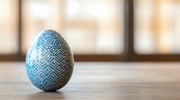 Decorative Easter egg painted in blue and white geometric pattern standing on wooden surface against blurred warm background. Seasonal holiday concept.