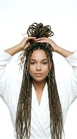 Young woman with medium brown skin tone wearing white button-up shirt, styling long braided hair with hands raised above head against white background for beauty and fashion content.