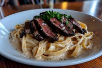Sliced medium-rare steak served on creamy fettuccine pasta garnished with fresh parsley, black pepper and sauce in white plate, restaurant quality meal.
