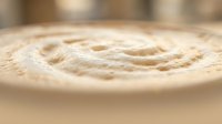 Creamy beige swirl texture with soft peaks and valleys, resembling whipped cream, frosting, or cosmetic product surface for culinary and beauty industry applications.