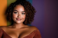 Young African American woman with natural curly hair and radiant smile wearing rust-colored off-shoulder top against colorful gradient background.