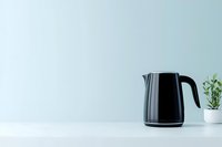 Modern black electric kettle on white counter against mint green wall with small potted plant, minimalist kitchen scene for contemporary lifestyle design.