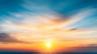 Dramatic sunset sky with vibrant orange and blue colors, soft wispy clouds creating ethereal atmosphere against glowing sun on horizon. Perfect for nature backgrounds.