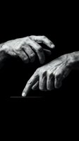 Elderly wrinkled hands reaching out on black background, monochrome artistic portrait showing aging process and human connection in dramatic lighting.