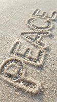 Word BEACH written in sandy shore with colorful shell pieces filling the letters, close-up summer vacation concept on natural textured sand background.