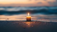 Glowing candle on sandy beach at sunset with blurred ocean waves in background creates peaceful atmospheric scene for meditation and mindfulness.