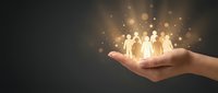 Human hand holding glowing group of people figures with sparkling light effects representing teamwork, leadership and community connection concepts.