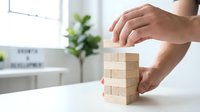 Business professional carefully stacking wooden blocks in modern office environment representing strategic planning and growth concepts.