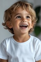 Joyful young child with curly blonde hair wearing white t-shirt expressing genuine happiness and wonder while looking up with bright smile and sparkling eyes.