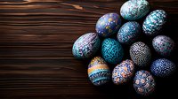 Colorfully decorated Easter eggs with intricate patterns in blue, turquoise and pink tones arranged on dark wooden background. Traditional holiday celebration art.