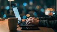 Professional working on laptop computer at night with colorful city lights bokeh background creating productive atmosphere for remote work and business.