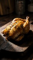 Golden roasted whole chicken with herbs on wooden cutting board in rustic kitchen setting with steam rising from hot cooked poultry for dinner preparation.