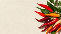 Fresh colorful chili peppers with green leaves arranged on light beige linen textile background, corner composition with copy space for food design.