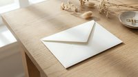 White envelope on wooden table with dried flowers and natural lighting for correspondence and mailing concepts.