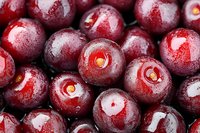 Fresh ripe dark red cherries with water drops, macro shot showing natural texture and glossy surface of sweet summer fruits for food background.