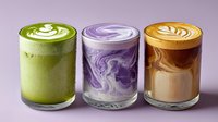 Colorful trio of specialty lattes in clear glasses - matcha green tea, purple taro, and classic caramel - showcasing intricate latte art on creamy foam surfaces.