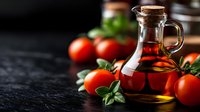 Fresh ripe tomatoes and glass bottle with olive oil on dark rustic background with basil leaves, selective focus and copy space for food design.