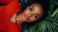Young African American woman in red outfit lying among tropical palm leaves, with dramatic lighting and vibrant contrast between red fabric and green foliage.