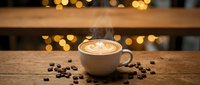 Cappuccino with latte art in white cup surrounded by coffee beans on wooden table with warm bokeh lights in background.