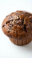 Freshly baked chocolate muffin with melted chips and cracked top in brown paper wrapper, ideal for bakery, food, and dessert marketing materials.