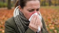 Woman with cold or flu symptoms blowing nose with tissue in autumn park. Seasonal illness, healthcare and wellness concept for medical campaigns.
