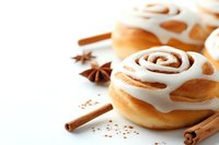 Fresh cinnamon rolls with white cream cheese frosting, decorated with cinnamon sticks and star anise on light background, selective focus, copy space.