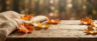 Cozy autumn scene with burlap sack and colorful fall leaves on rustic wooden table with warm bokeh background for seasonal harvest decorating.