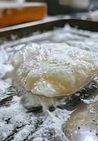 Fresh raw dough covered in flour on dark surface, macro shot showing texture and bubbles in baking preparation process.