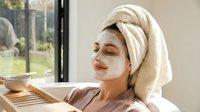 Young woman relaxing with facial mask and towel wrapped hair enjoying spa treatment at home for skincare routine and wellness self-care.