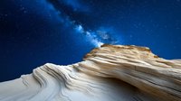 Layered sandstone rock formation against starry night sky with bright Milky Way galaxy, natural geological patterns in desert landscape at night.