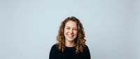 Young cheerful woman with curly brown hair laughing joyfully in black sweater against light gray background for lifestyle and portrait projects.