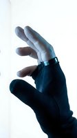 Hand wearing black compression glove with metal ring support brace for arthritis pain relief and joint stability on white background.