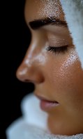 Close-up profile of Asian woman's face with dewy, glowing skin and long eyelashes against dark background, showcasing natural beauty and skincare results.