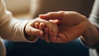 Tender moment of adult hand gently holding tiny baby hand showing love, care and protection in warm soft lighting for family and parenting concepts.