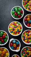 Colorful assorted candies and sweets in white bowls on dark slate background for party treats, confectionery display and dessert presentation.